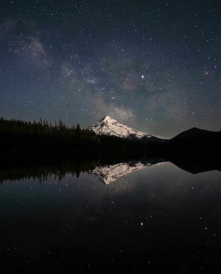 Mountain being mirrored on lake at night with stars and snow on the pct